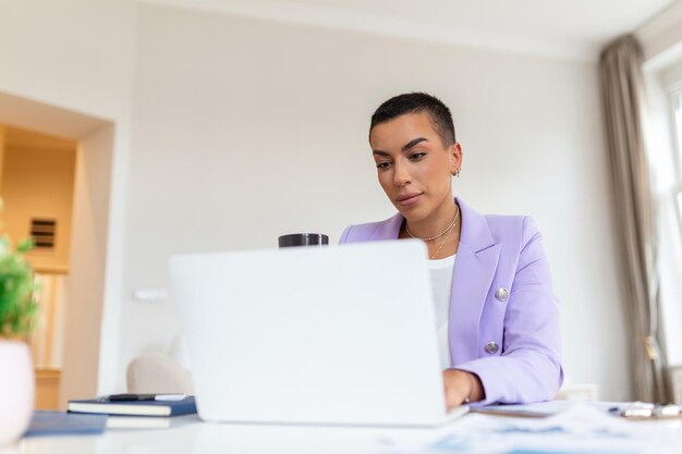 Junge afroamerikanische Geschäftsfrau, die von zu Hause aus mit einem Laptop arbeitet und lächelnd eine Tasse Kaffee genießt