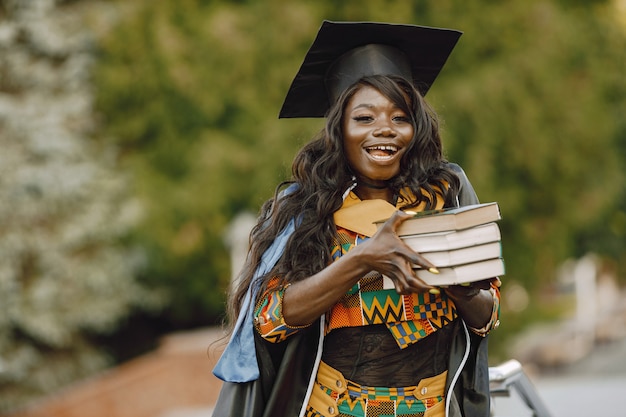 Junge afroamerikanische Studentin in schwarzem Abschlusskleid gekleidet. Campus als Hintergrund