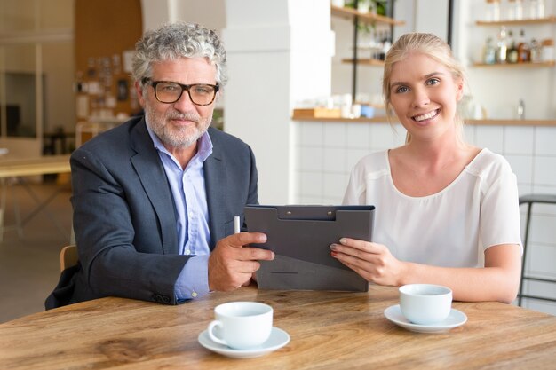 Junge Agentin und reife Kundentreffen bei einer Tasse Kaffee bei der Zusammenarbeit, am Tisch sitzen, Dokumente halten,