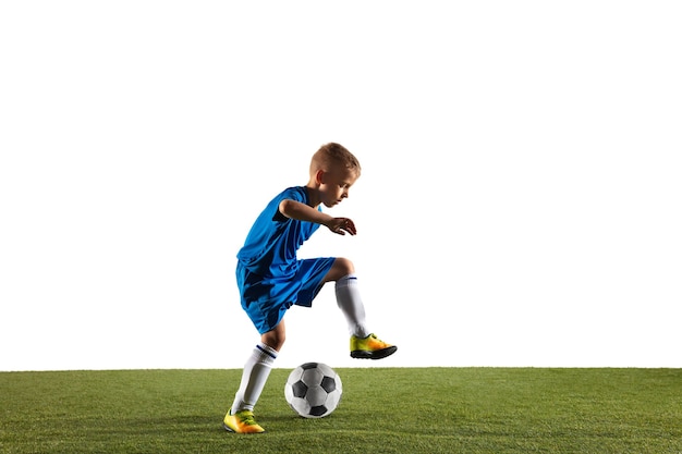 Junge als Fußball- oder Fußballspieler in Sportbekleidung, die eine Finte oder einen Tritt mit dem Ball für ein Tor auf weißem Hintergrund macht.