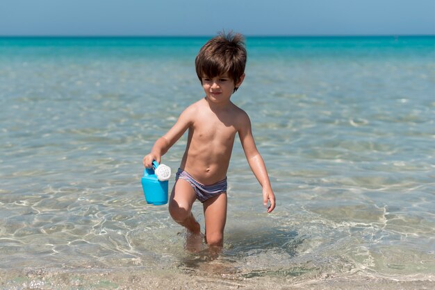 Junge am Strand, der Gießkanne hält