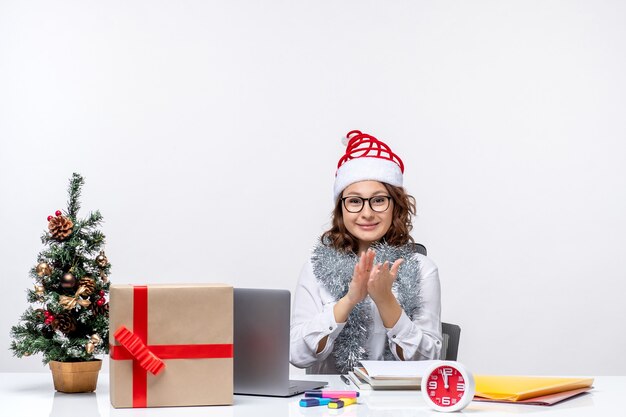 Junge Arbeiterin der Vorderansicht, die vor ihrem Arbeitsplatz sitzt und auf weißem Hintergrund lächelt