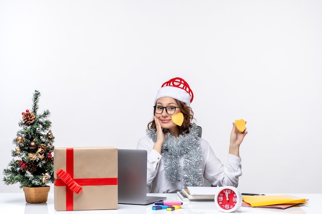 Junge Arbeiterin der Vorderansicht, die vor ihrem Platz sitzt, der Aufkleber auf dem weißen Bodengeschäftsbüroarbeits-Weihnachtsjobdame hält