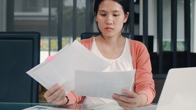 Junge asiatische Aufzeichnungen der schwangeren Frau über Einkommen und Ausgaben zu Hause. Muttermädchen glücklich unter Verwendung des Laptopaufzeichnungsbudgets, Steuer, Finanzdokument, elektronischer Geschäftsverkehr, der zu Hause im Wohnzimmer arbeitet.