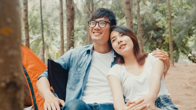 Junge asiatische Camper-Paare sitzen in Stühlen von Zelt im Wald. Männliche und weibliche Reisende, die sich an einem Sommertag auf dem Campingplatz entspannen und unterhalten?