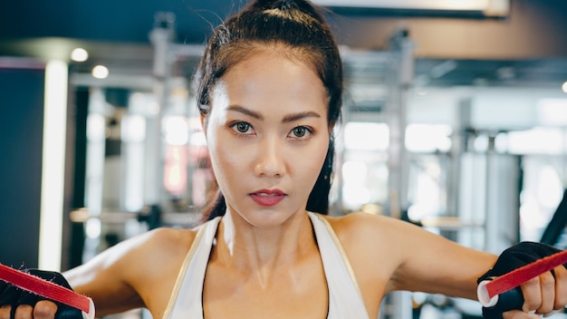 Junge asiatische Dame, die Übungsmaschinen-Kabelkreuzung in der Fitnessklasse tut