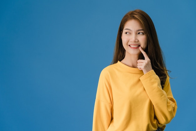 Junge asiatische Dame, die Lächeln, positiven Ausdruck zeigt, gekleidet in lässiger Kleidung und Spaßgefühl isoliert auf blauem Hintergrund. Glückliche entzückende frohe Frau freut sich über Erfolg. Gesichtsausdruck Konzept.