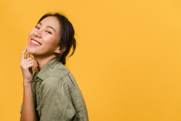 Junge asiatische Dame mit positivem Ausdruck, breites Lächeln, gekleidet in Freizeitkleidung über gelber Wand. Glückliche entzückende frohe Frau freut sich über Erfolg. Gesichtsausdruck Konzept.