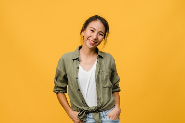 Junge asiatische Dame mit positivem Ausdruck, breites Lächeln, gekleidet in Freizeitkleidung über gelber Wand. Glückliche entzückende frohe Frau freut sich über Erfolg. Gesichtsausdruck Konzept.