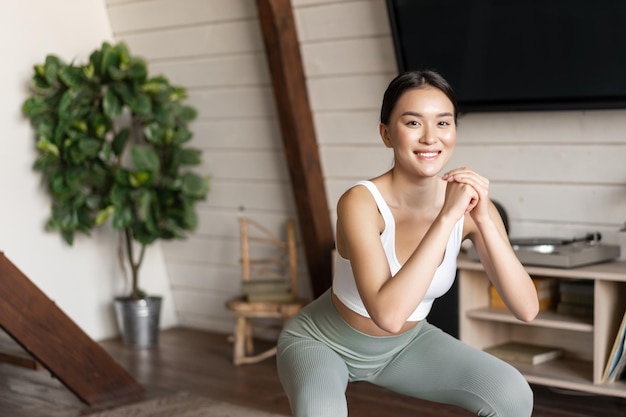 Junge asiatische Fitnessfrau mit gesundem, fittem Körper macht Kniebeugen am Morgentraining in Activewear-Stan...