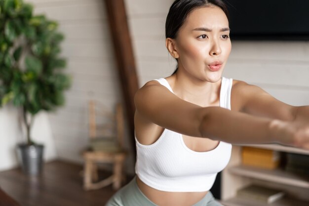 Junge asiatische Fitnessfrau mit gesundem, fittem Körper macht Kniebeugen am Morgentraining in Activewear-Stan...