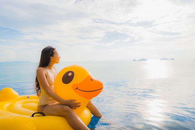 Junge asiatische Frau des Porträts auf gelber Ente des aufblasbaren Schwimmers um Swimmingpool im Freien im Hotel und im Erholungsort