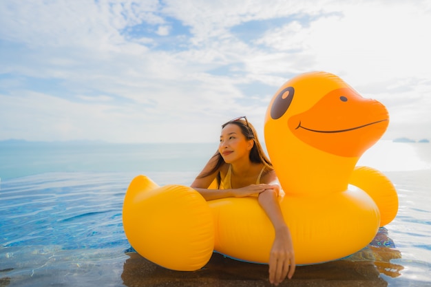 Kostenloses Foto junge asiatische frau des porträts auf gelber ente des aufblasbaren schwimmers um swimmingpool im freien im hotel und im erholungsort