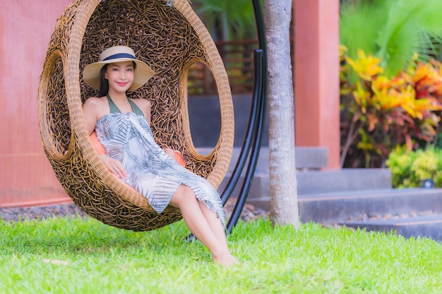 Junge asiatische Frau des Porträts, die auf Schwingenstuhl im Garten sitzt