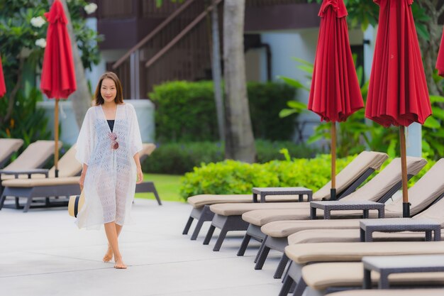 Junge asiatische Frau des Porträts entspannen sich das Lächeln, das um Swimmingpool im Freien im Hotelerholungsort mit Seeozeanblick glücklich ist