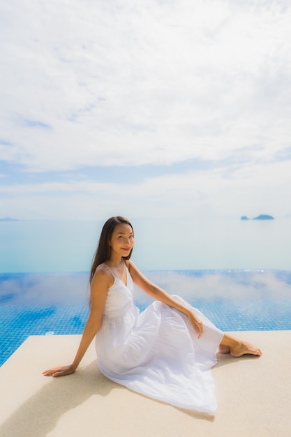 Junge asiatische Frau des Porträts entspannen sich das Lächeln, das um Swimmingpool im Hotel und im Erholungsort glücklich ist