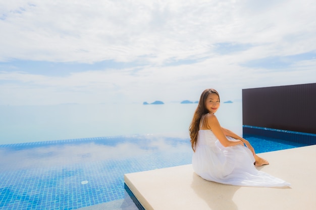 Junge asiatische Frau des Porträts entspannen sich das Lächeln, das um Swimmingpool im Hotel und im Erholungsort glücklich ist