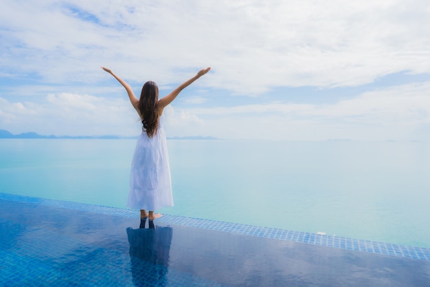 Junge asiatische Frau des Porträts entspannen sich das Lächeln, das um Swimmingpool im Hotel und im Erholungsort glücklich ist