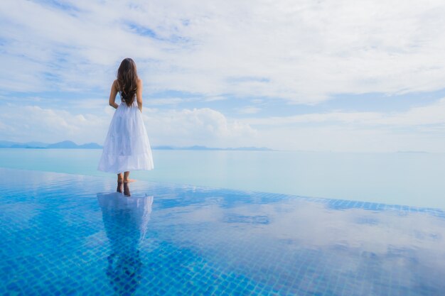 Junge asiatische Frau des Porträts entspannen sich das Lächeln, das um Swimmingpool im Hotel und im Erholungsort glücklich ist