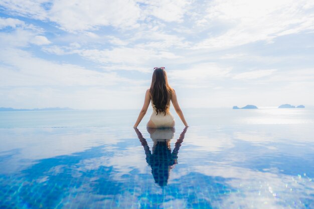 Junge asiatische Frau des Porträts entspannen sich das Lächeln, das um Swimmingpool im Hotel und im Erholungsort glücklich ist