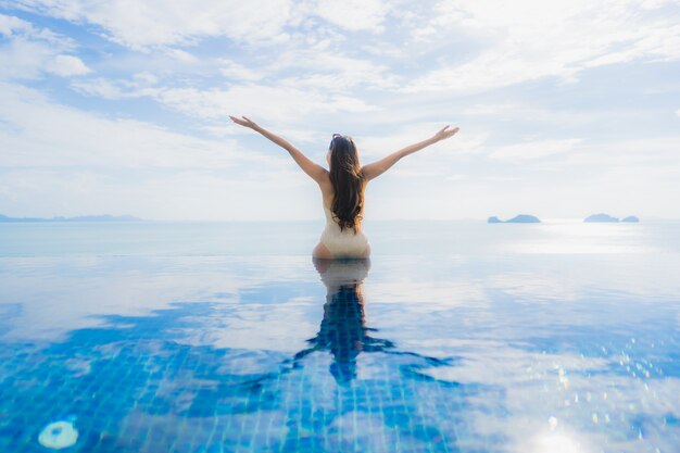 Junge asiatische Frau des Porträts entspannen sich das Lächeln, das um Swimmingpool im Hotel und im Erholungsort glücklich ist