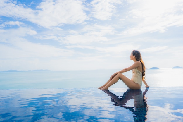 Junge asiatische Frau des Porträts entspannen sich das Lächeln, das um Swimmingpool im Hotel und im Erholungsort glücklich ist