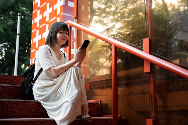 Kostenloses Foto junge asiatische frau, die draußen ihr smartphone überprüft