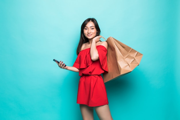 Junge asiatische Frau, die Einkaufstaschen und Textnachrichten am Telefon lokalisiert auf grüner Wand trägt