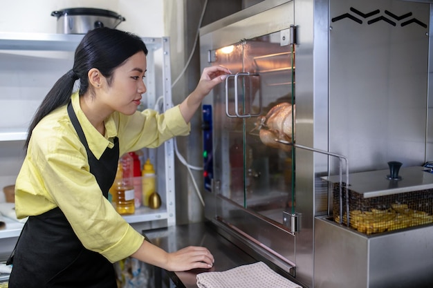 Junge asiatische Frau, die in der Küche arbeitet und die Ofentemperatur reguliert