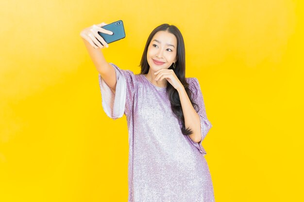 junge asiatische Frau, die mit Smartphone auf Gelb lächelt