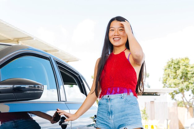 Junge asiatische Frau, die nahes Auto steht und Haar berührt