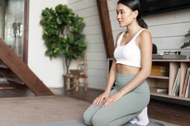 Junge asiatische Frau trainiert zu Hause, meditiert oder macht Yoga-Übungen im Wohnzimmer mit Sport...