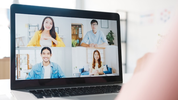 Kostenloses Foto junge asiatische geschäftsfrau, die laptop verwendet, spricht mit kollegin über plan in videoanrufbesprechung, während sie von zu hause aus im wohnzimmer arbeitet.