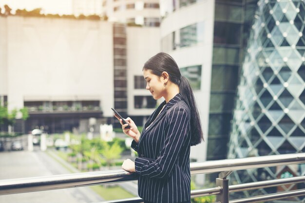 Junge asiatische Geschäftsfrau mit mobilen smartphone.Young weiblichen professionellen in der Stadt vor der großen Gebäude.