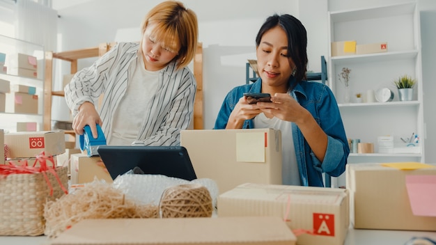 Junge asiatische Geschäftsfrauen, die Handy verwenden, erhalten Bestellung und überprüfen Produkt auf Lager arbeiten zu Hause Büro