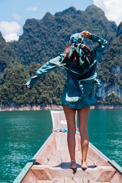 Junge asiatische glückliche Frau Blogger-Tourist in Seidenanzug und Schal und Sonnenbrille im Urlaub reisen um Thailand auf asiatischem Boot, Khao Sok Nationalpark.