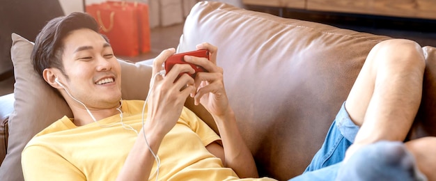 Junge asiatische männliche Hand, die Smartphone-Spiele online beiläufig und in der Freizeit spielt, aufregend und fröhlich auf dem Sofa am Wochenende zu Hause Quarantäne-Aktivitätsideen-Konzept