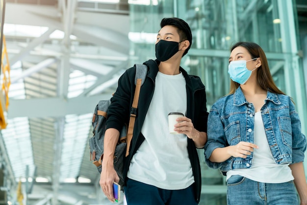 Junge asiatische männliche und weibliche paar touristen ziehen gepäck, das nach der ankunft durch den flur geht zwei asiaten reisende tragen gesichtsmaske virenschutz sicherheit reiseideen konzept