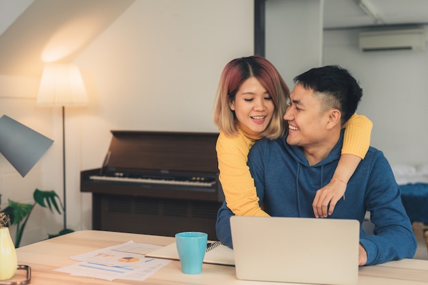 Junge asiatische Paare, die Finanzen, ihre Bankkonten unter Verwendung der Laptop-Computers wiederholen
