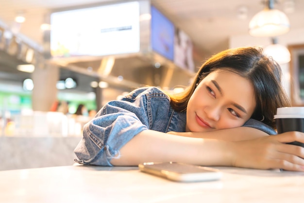 Junge asiatische reisende frau sitzen entspannen gesichtsausdruck hand benutzen smartphone warten auf bordzeit im café-restaurant am flughafen-abflugterminal