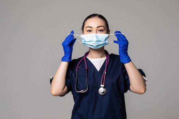 Junge asiatische Ärztin trägt medizinische Maske mit Blick auf die Vorderseite isoliert auf weißer Wand