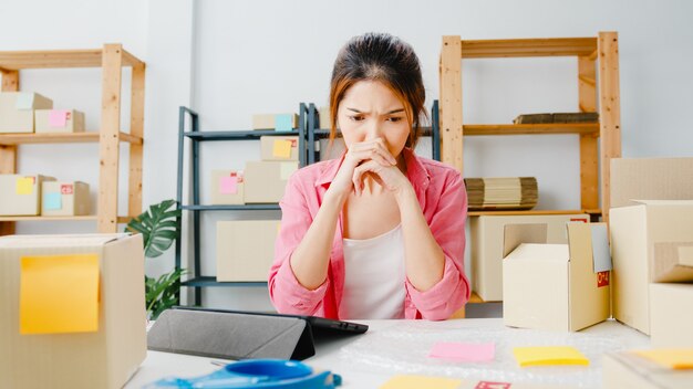 Junge asiatische Unternehmer Geschäftsfrau überprüfen Produktbestellung auf Lager, mit Tablet harte Arbeit Überlastung im Home Office. Kleinunternehmer, Online-Marktzustellung, freiberufliches Lifestyle-Konzept.