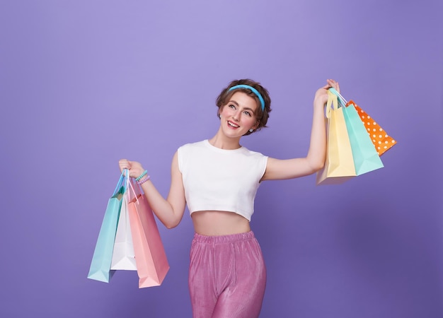 junge attraktive Einkäuferin mit Einkaufstasche, isoliert auf lila Hintergrund