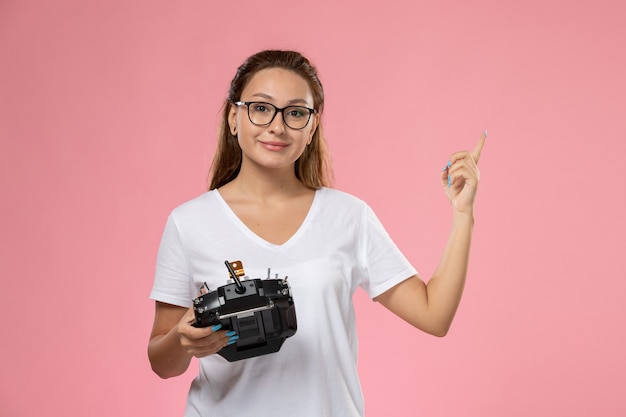 Junge attraktive Frau der Vorderansicht im weißen T-Shirt mit unzufriedenem Ausdruck, der Fernbedienung auf dem rosa Schreibtisch hält