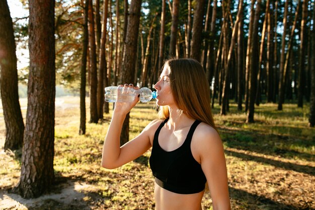 junge attraktive Frau, die ein Wasser von der Flasche nach dem Trainieren im Park trinkt