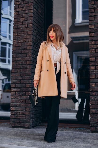 Junge attraktive Frau im beigen Mantel posiert auf der Straße