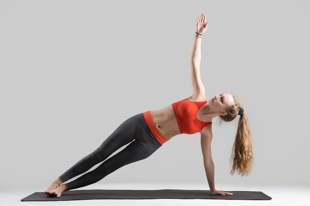 Junge attraktive Frau stehend in Side Plank Pose, grau Studio