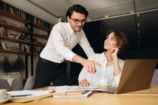 Junge attraktive Geschäftskollegen, die gerne an neuen Projekten mit Laptop und Papieren im modernen Büro arbeiten