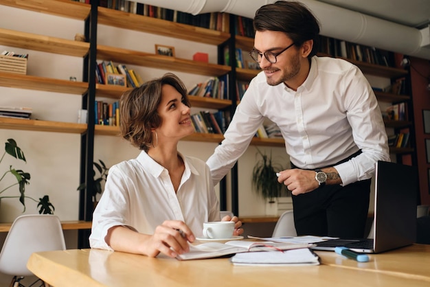 Junge attraktive Geschäftskollegen, die sich freudig anschauen und gemeinsam an einem neuen Projekt in einem modernen Büro arbeiten