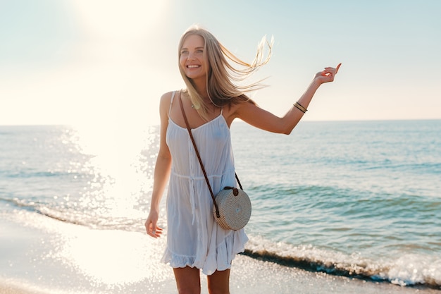 Junge attraktive glückliche Frau, die durch sonnigen Sommermode-Stil des Seestrandes sich dreht